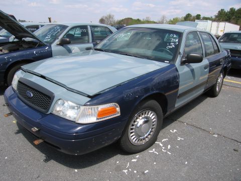 2001 Ford Crown Victoria - A two-tone Ford Crown Victoria sits in a lot with other vehicles, some with hoods open.