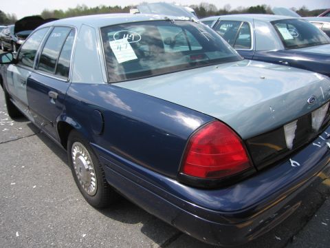 2001 Ford Crown Victoria - A two-tone Ford Crown Victoria is parked in a lot with other vehicles, showing its rear quarter panel and window tag.