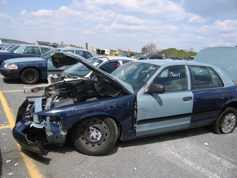 2001 Ford Crown Victoria - This two-tone police car, possibly a Ford Crown Victoria, is in a junkyard with its hood and trunk open, revealing damage and VIN numbers o…