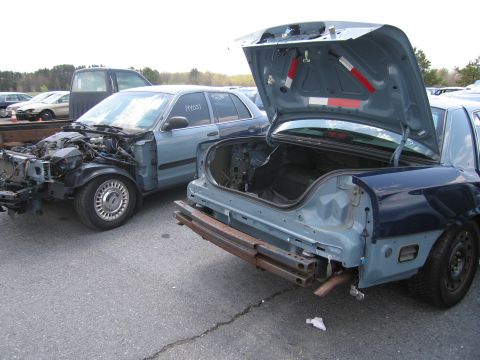 2001 Ford Crown Victoria - Two Ford Crown Victorias in a state of disrepair, one with its trunk open and the other missing its front end.