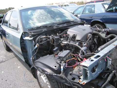 2001 Ford Crown Victoria - The engine compartment of a light blue 2001 Ford Crown Victoria is visible, with the hood open and front end damaged.