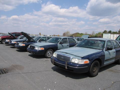 2001 Ford Crown Victoria - Several Ford Crown Victoria police cars are parked in a row under a cloudy sky.