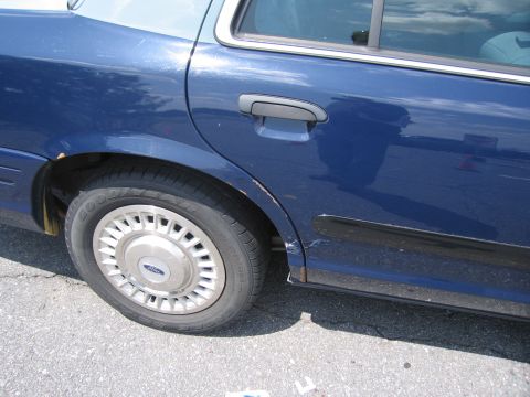 2001 Ford Crown Victoria - Side view of a blue 2001 Ford Crown Victoria showing minor body damage and a two-tone paint scheme on the roof.