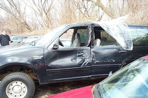 2001 Ford Crown Victoria - This black SUV sustained heavy damage to its driver's side, with the doors severely dented and the passenger window covered by plastic shee…