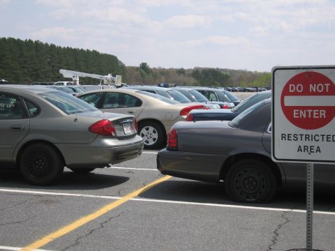 2001 Ford Crown Victoria - A dark-colored police car with a flat rear tire is parked in a lot, next to other vehicles, under a cloudy sky.