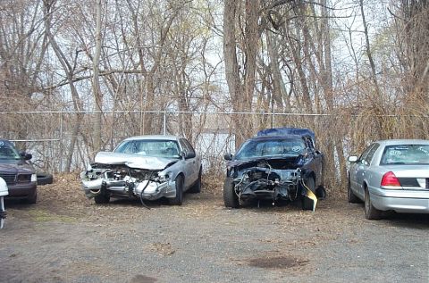 2001 Ford Crown Victoria - Two heavily damaged Ford Crown Victoria police cars sit in a lot, likely after an accident.