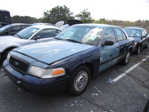 2001 Ford Crown Victoria - A 2001 Ford Crown Victoria is parked in an outdoor lot with other vehicles, showing some damage and mismatched paint panels.