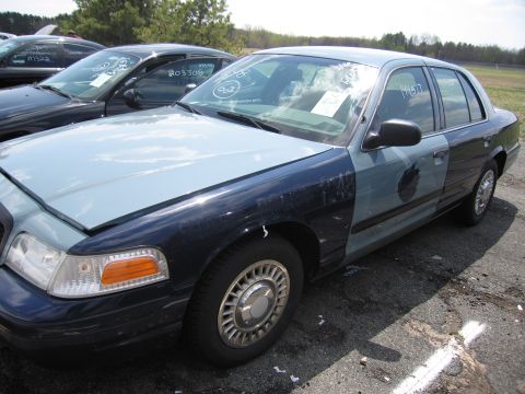 2001 Ford Crown Victoria - A two-tone 2001 Ford Crown Victoria is parked in a lot with other vehicles, showing some damage to its body panels.