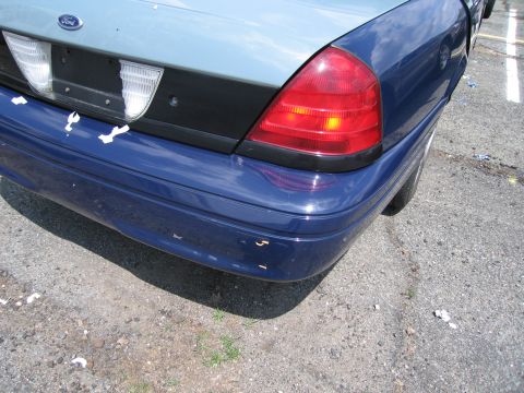 2001 Ford Crown Victoria - The rear of a blue Ford Crown Victoria shows a dented bumper and a two-tone paint job.