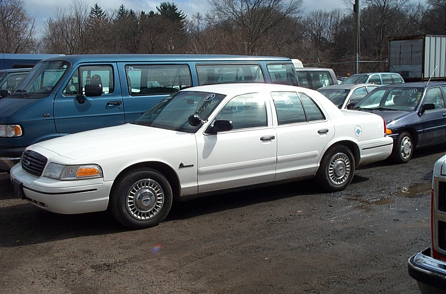 White 2001 Ford Crown Victoria sedan parked on dirt lot, side view