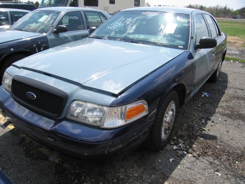 2001 Ford Crown Victoria - A two-tone Ford Crown Victoria is parked in a lot with other vehicles. Text is visible on the windshield.