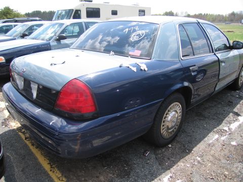 2001 Ford Crown Victoria - A 2001 Ford Crown Victoria is parked in a lot with other vehicles, showing some wear and tear.