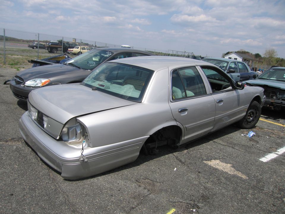 Silver Mercury Grand Marquis sedan with missing wheel in a salvage lot