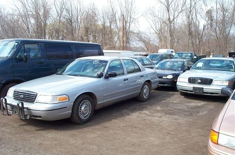 2001 Ford Crown Victoria - A silver 2001 Ford Crown Victoria is parked in a lot with several other cars and a van.