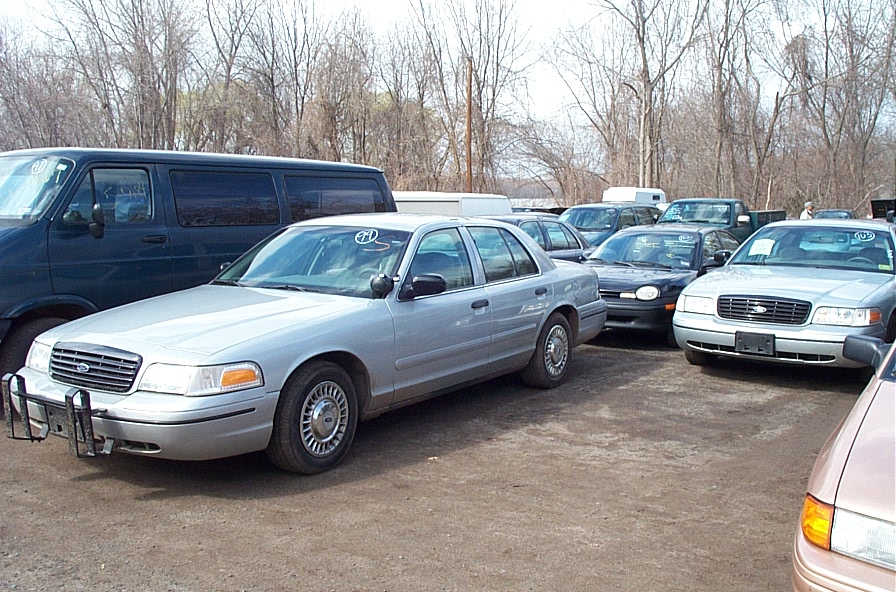 Silver 2001 Ford Crown Victoria with a push bumper, parked outdoors with other vehicles
