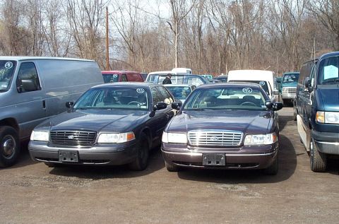 2001 Ford Crown Victoria - Two Ford Crown Victorias are parked side-by-side in an outdoor lot with other vehicles visible in the background.