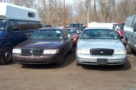 2001 Ford Crown Victoria - Two Ford Crown Victorias are parked in an outdoor lot with other vehicles visible.