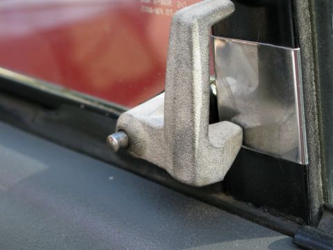 1991 Ford F-150 - Close-up of a gray textured door handle mechanism and a chrome trim piece on a vehicle. The red paint of the vehicle's body is visible thro…