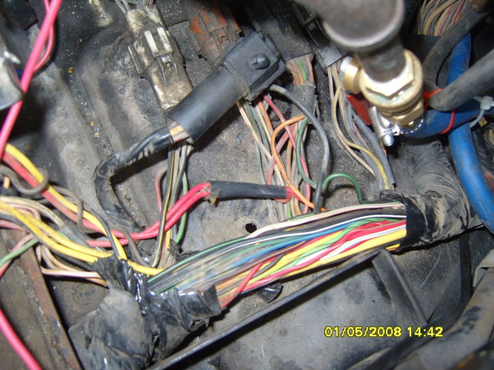 Close-up of a messy vehicle wiring harness with many colored wires and tape.