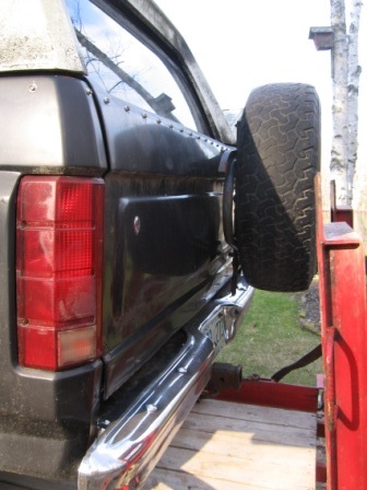 1993 Ford Bronco - Close-up of the driver-side rear corner of a black Ford Bronco on a trailer, showing the multi-segment tail light, dented and creased rear…