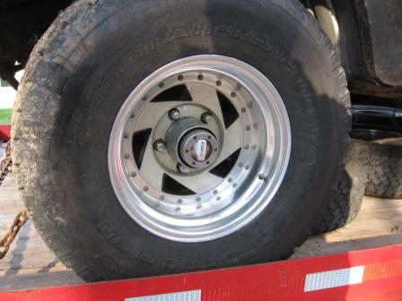 1993 Ford Bronco - Close-up of a polished aluminum five-slot wheel with a riveted outer lip, mounted on a BFGoodrich All-Terrain T/A tire and sitting on a red…