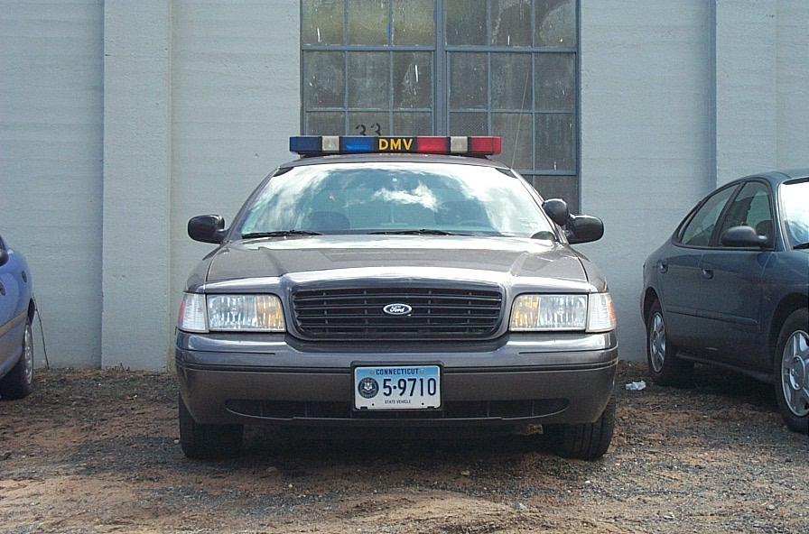 Front view of a 2001 Ford Crown Victoria police car with a DMV light bar. Another car is parked to the right