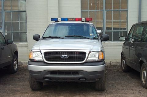 2001 Ford Crown Victoria - A silver Ford Expedition with a light bar is parked in front of a building.