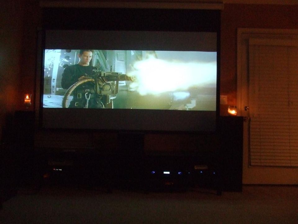 Movie scene of a man firing a machine gun projected onto a screen in a dark room.