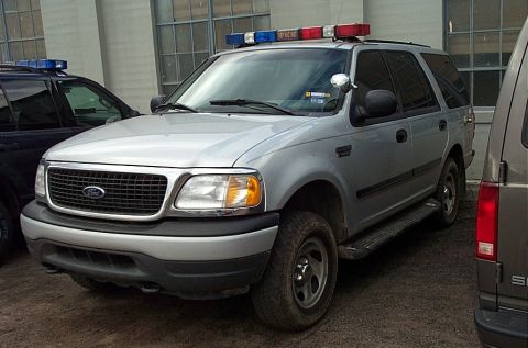 2001 Ford Crown Victoria - A silver Ford Expedition, likely from around 2001, is parked next to another vehicle, equipped with emergency lights on its roof.