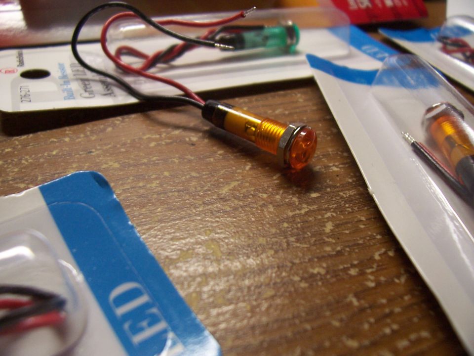 Several small LED indicator lights with wires in plastic packaging on a wooden surface.
