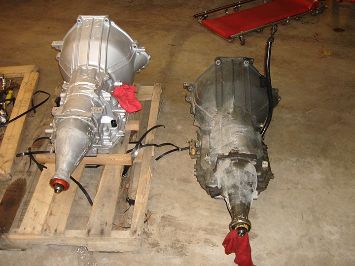 Two automatic transmissions, one silver and one dirty, side-by-side on a concrete floor.