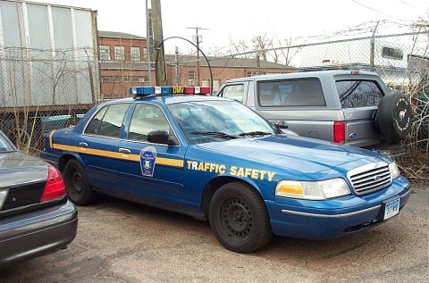 2001 Ford Crown Victoria - A blue police car with a light bar and 'TRAFFIC SAFETY' text is parked in an outdoor lot.