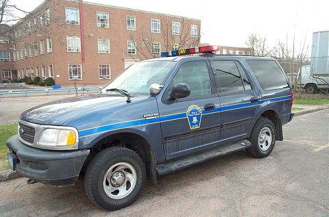 2001 Ford Crown Victoria - A blue Ford Expedition SUV, marked for DMV duty, is parked outside a brick building.