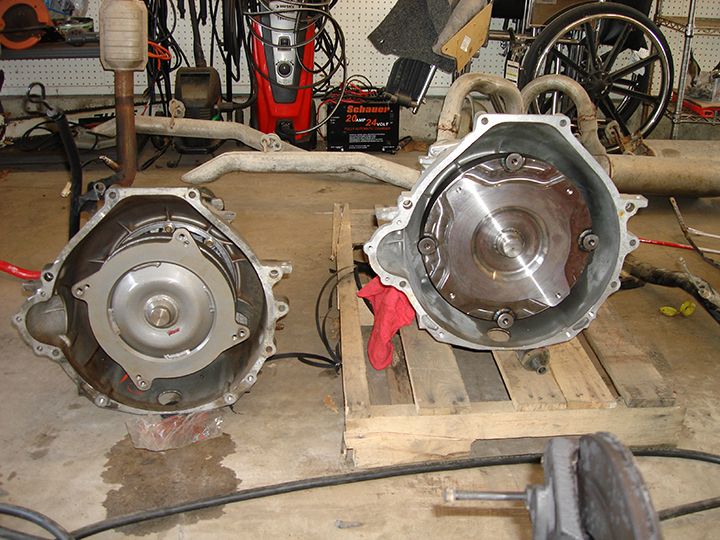 Two automatic transmissions with torque converters visible, one on a plastic sheet and the other on pallets.