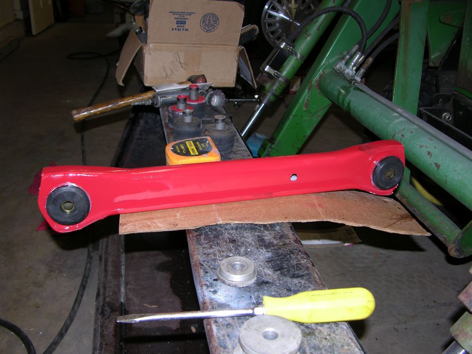 Red powder-coated suspension control arm with black bushings on a garage workbench