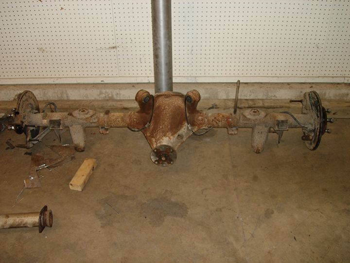 Rusty rear axle assembly with brake rotors lying on a garage floor during disassembly