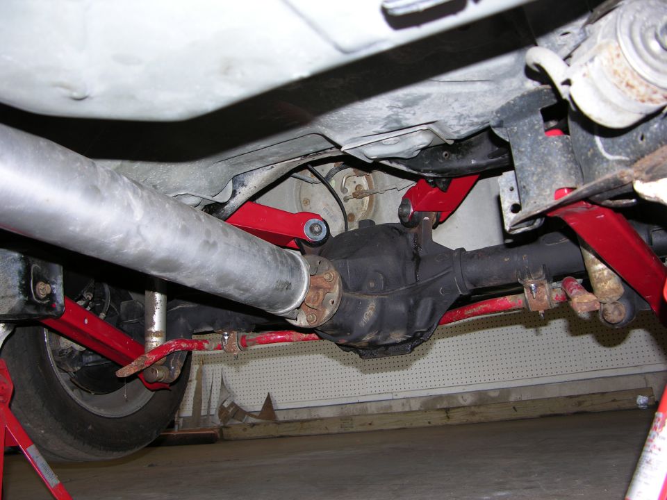 Underside rear axle with black differential, red control arms and silver exhaust pipe on lifted vehicle.