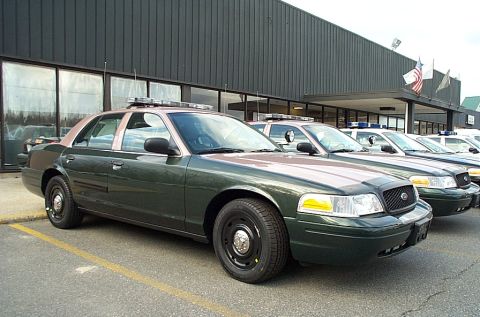 2001 Ford Crown Victoria - dark green Ford Crown Victoria police-package sedan with steel wheels parked among other patrol cars at a dealership.