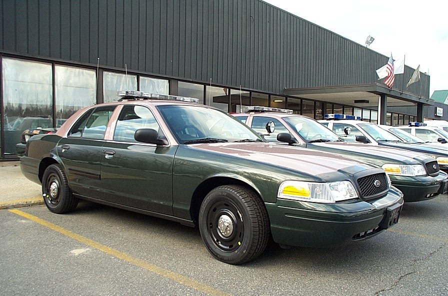 Dark green Ford Crown Victoria police sedan parked in a lot with other patrol cars at a dealer