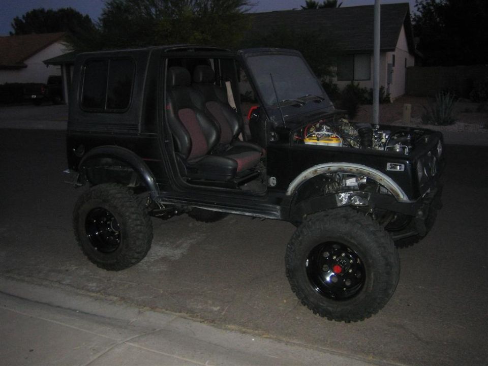 Flat-black lifted Suzuki Samurai, doors and hood removed, on black wheels and mud tires