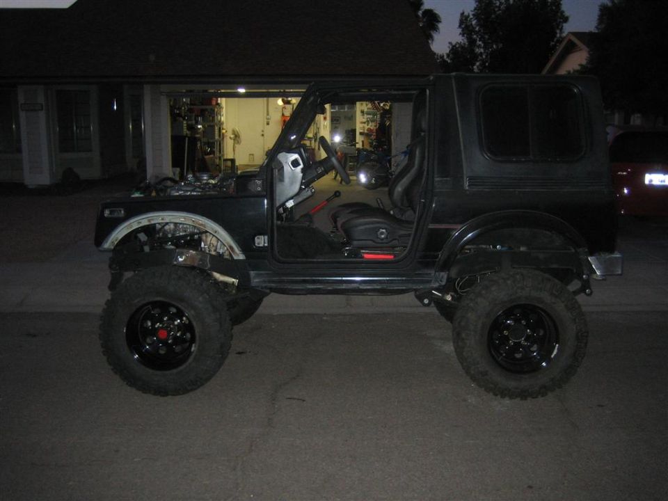 Black lifted Suzuki Samurai with doors removed, hood open, large tires, parked in driveway.