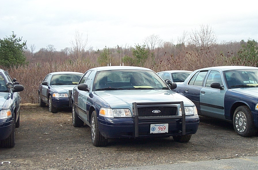 Several Ford Crown Victoria police cars parked in a lot. One has a push bar and license plate 969