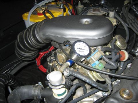 1987 Suzuki Samurai - A close-up view of the engine bay of a 1987 Suzuki Samurai, focusing on the carburetor and air intake system. A pressure gauge is attached…