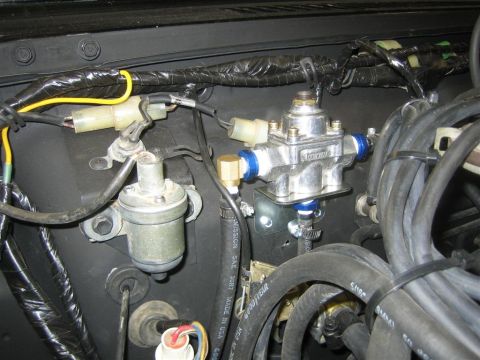 1987 Suzuki Samurai - A close-up view of engine bay components, including a silver fuel pressure regulator with blue accents and various hoses and wiring.