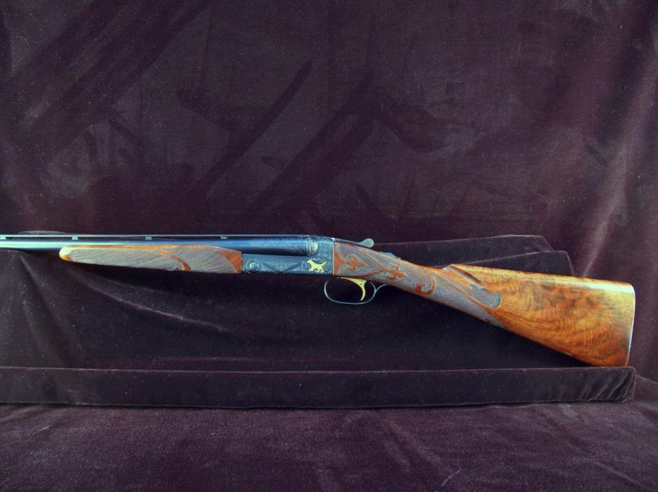 Engraved shotgun with wooden stock on dark velvet.