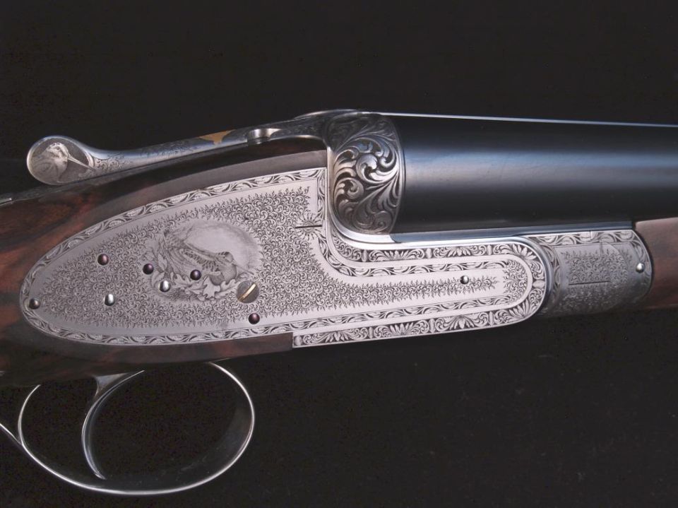 Close-up of engraved shotgun receiver and barrel with bird motif.