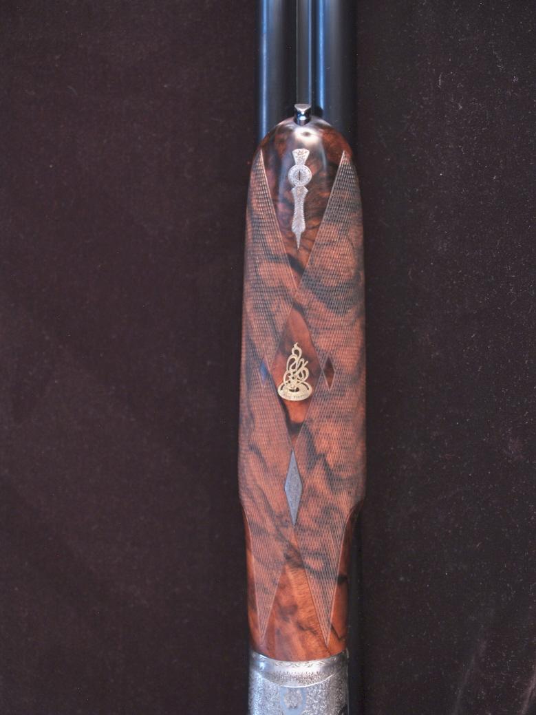 Close-up of a firearm grip with intricate wood grain and metal engraving.