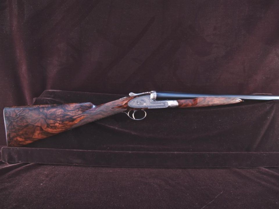 Vintage double-barreled shotgun with wood stock and engraved receiver.