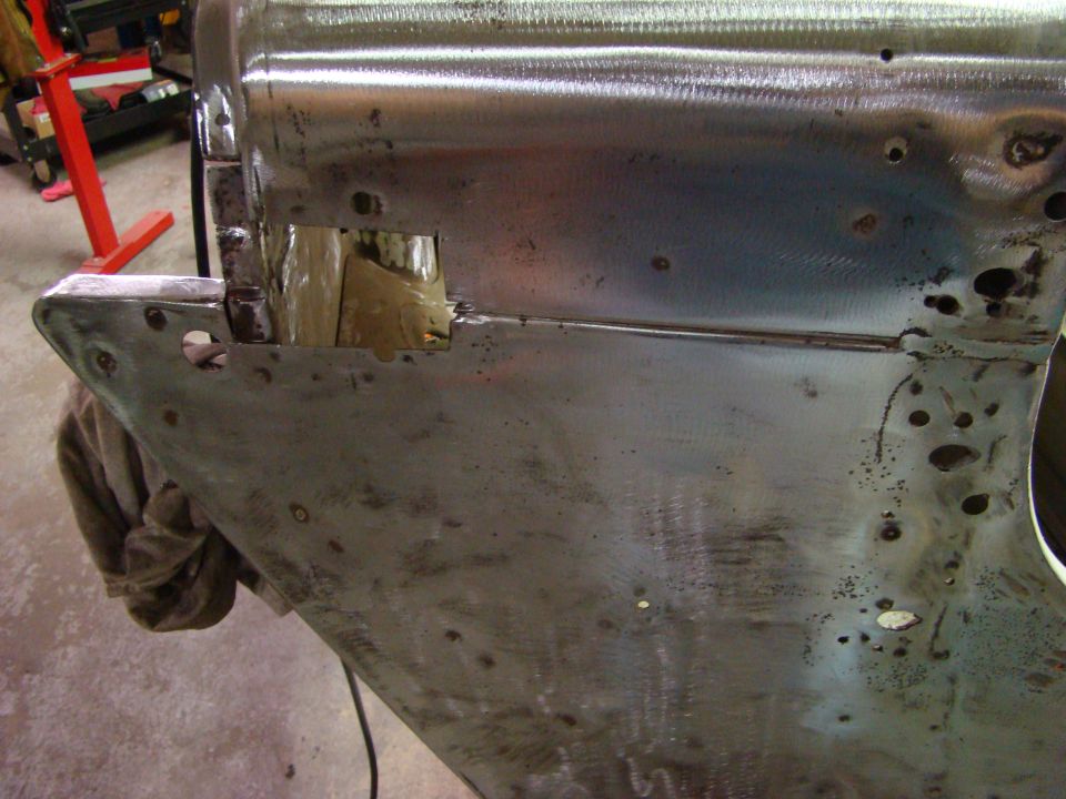 Bare metal car body panel with holes and welds, brown cloth draped.