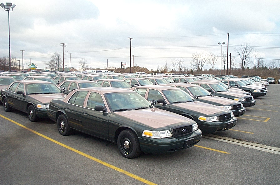 Row of two-tone green and tan Ford Crown Victoria police sedans parked in a fleet lot